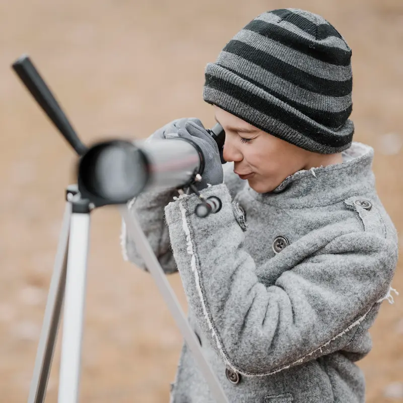 Un enfant regardant dans l'objectif de son télescope