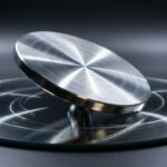Disque d'Euler métallique brossé en rotation sur une surface miroir, créant des reflets concentriques sur fond sombre.