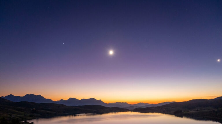 La planète Vénus brille intensément dans un ciel nocturne au-dessus d'un lac entouré de montagnes au crépuscule.