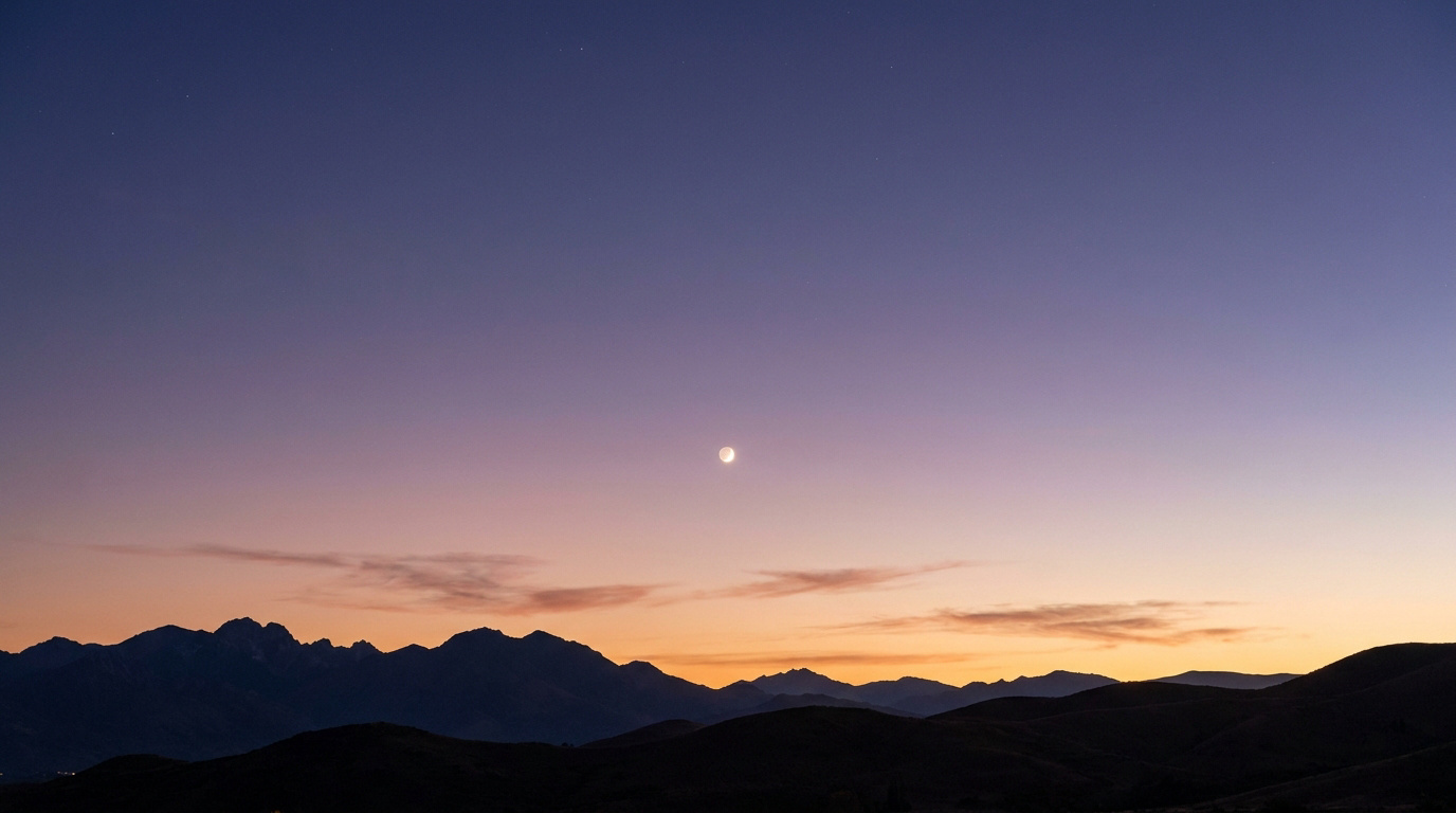 Un croissant de Lune brillant au-dessus d'une chaîne de montagnes lors d'un crépuscule aux nuances pourpres.